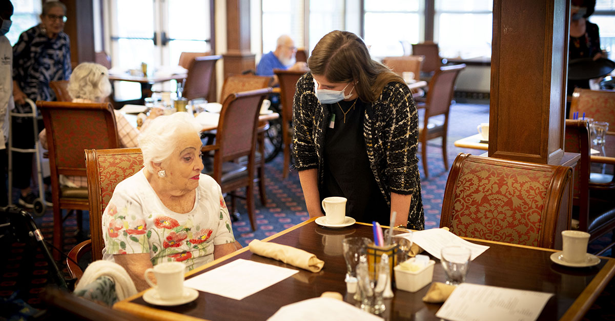 Employee and resident of Atria Senior Living talking in the dining room.